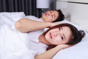 A woman covering her ears while a man with sleep apnea snores next to her